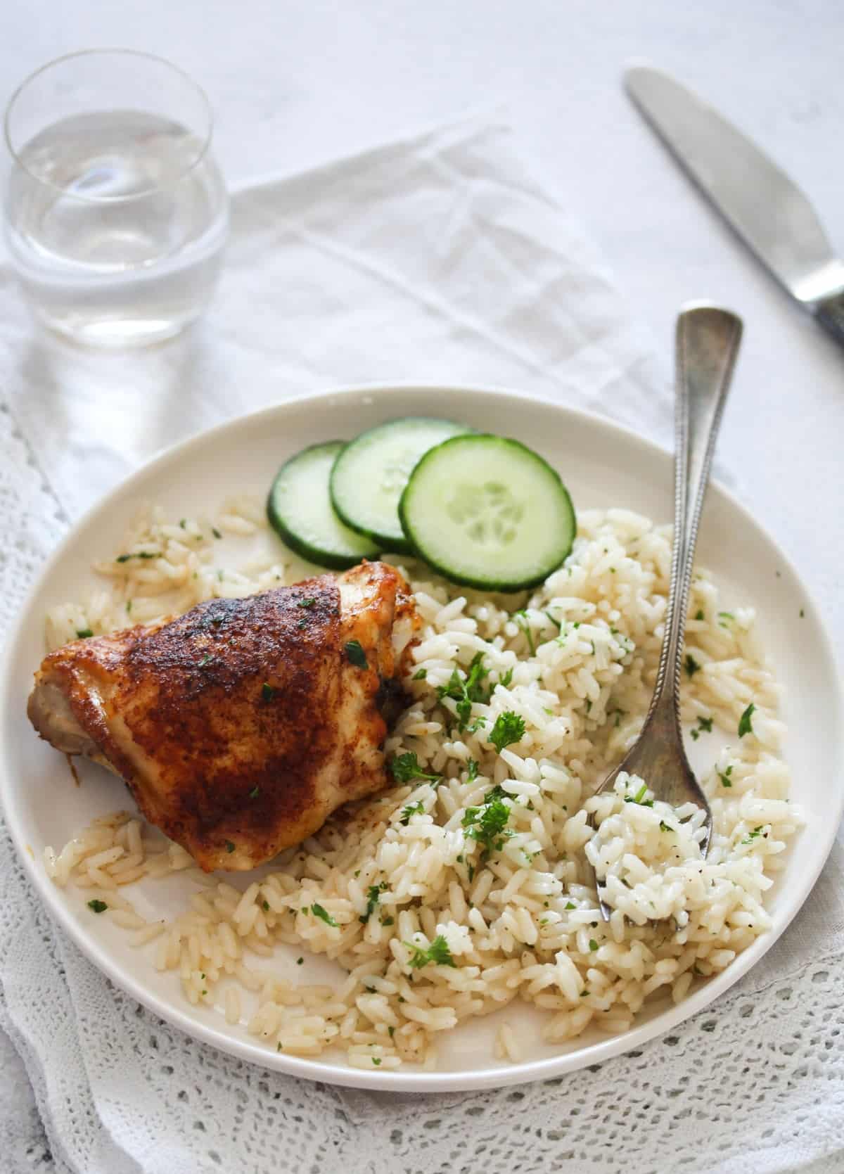 plate with rice, chicken thigh and cucumber slices.
