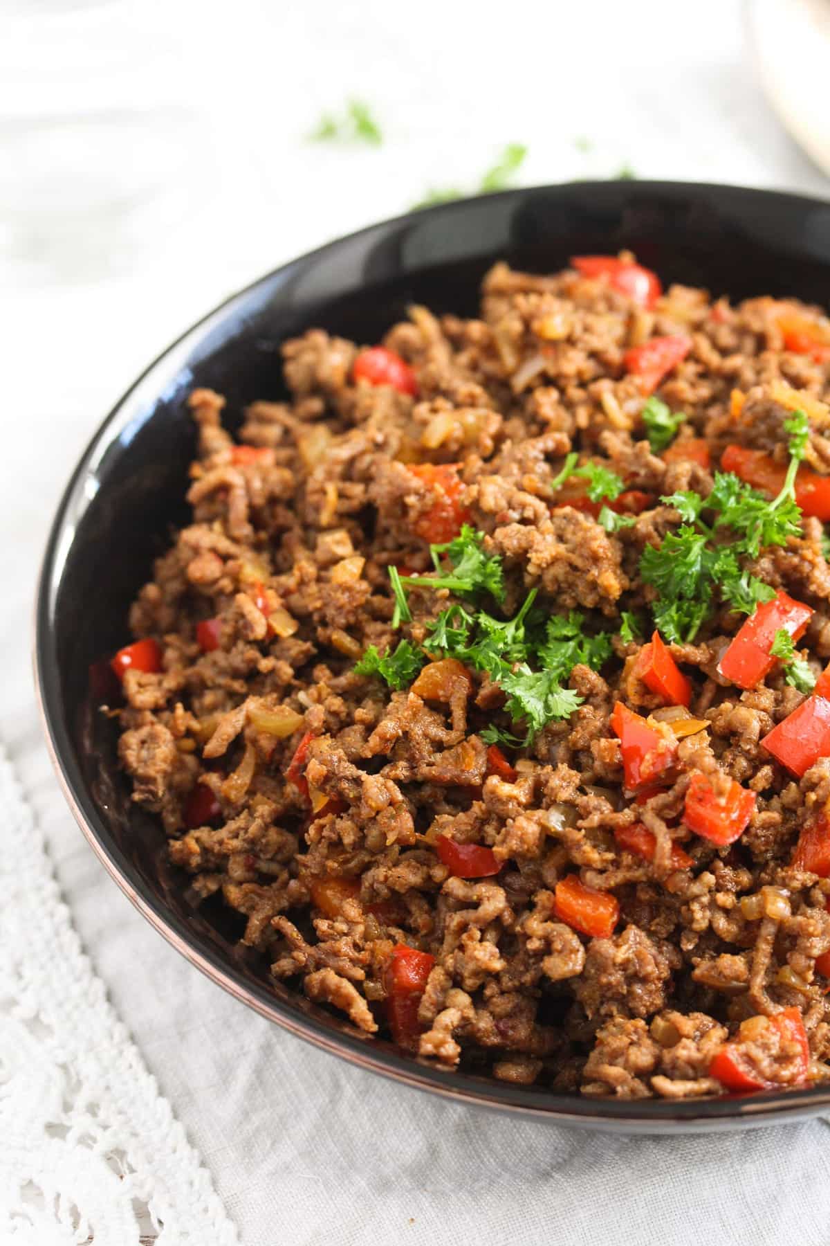 close up of a black bowl containing beef and red peppers with parsley on top.