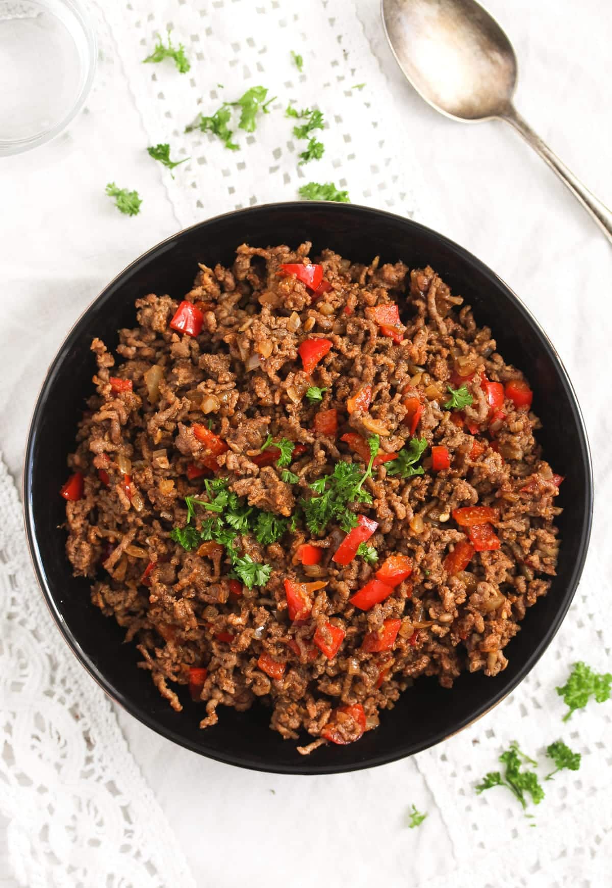 bowl with cooked ground meat with peppers and parsley with a spoon beside it.