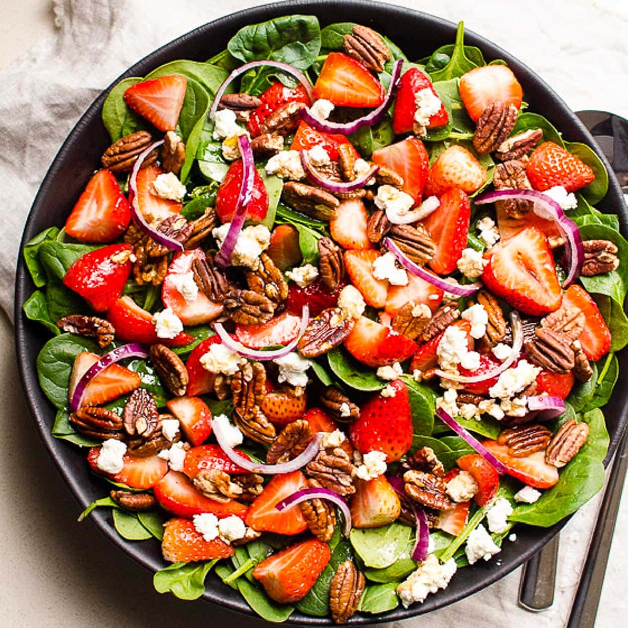 overhead view of a plate with strawberry spinach salad with nuts and red onions.