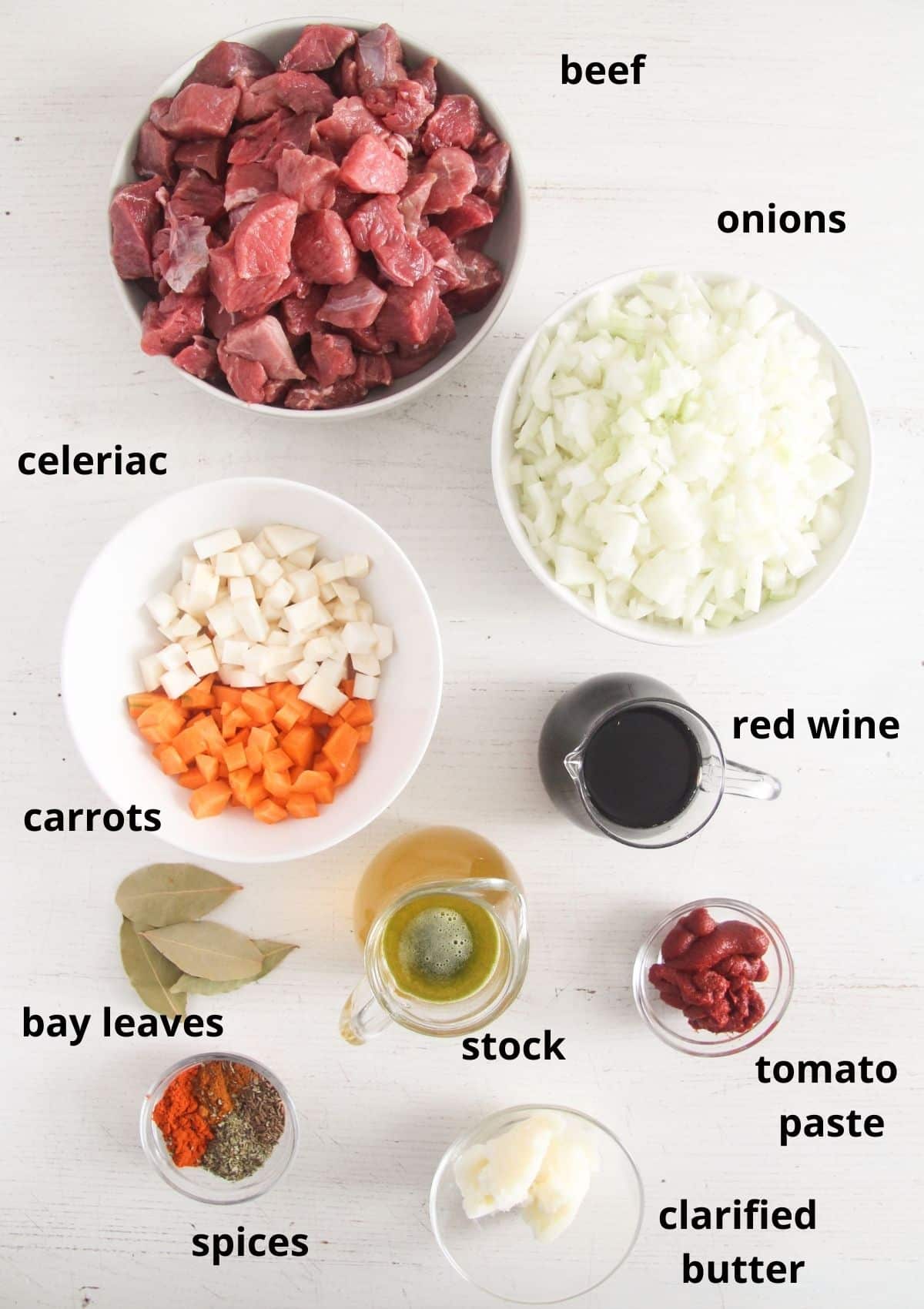 listed ingredients for making beef goulash on a white table.