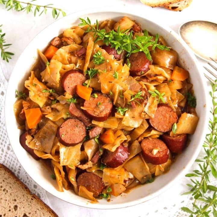 bowl full with slow cooker cabbage and sausages with thyme on top.