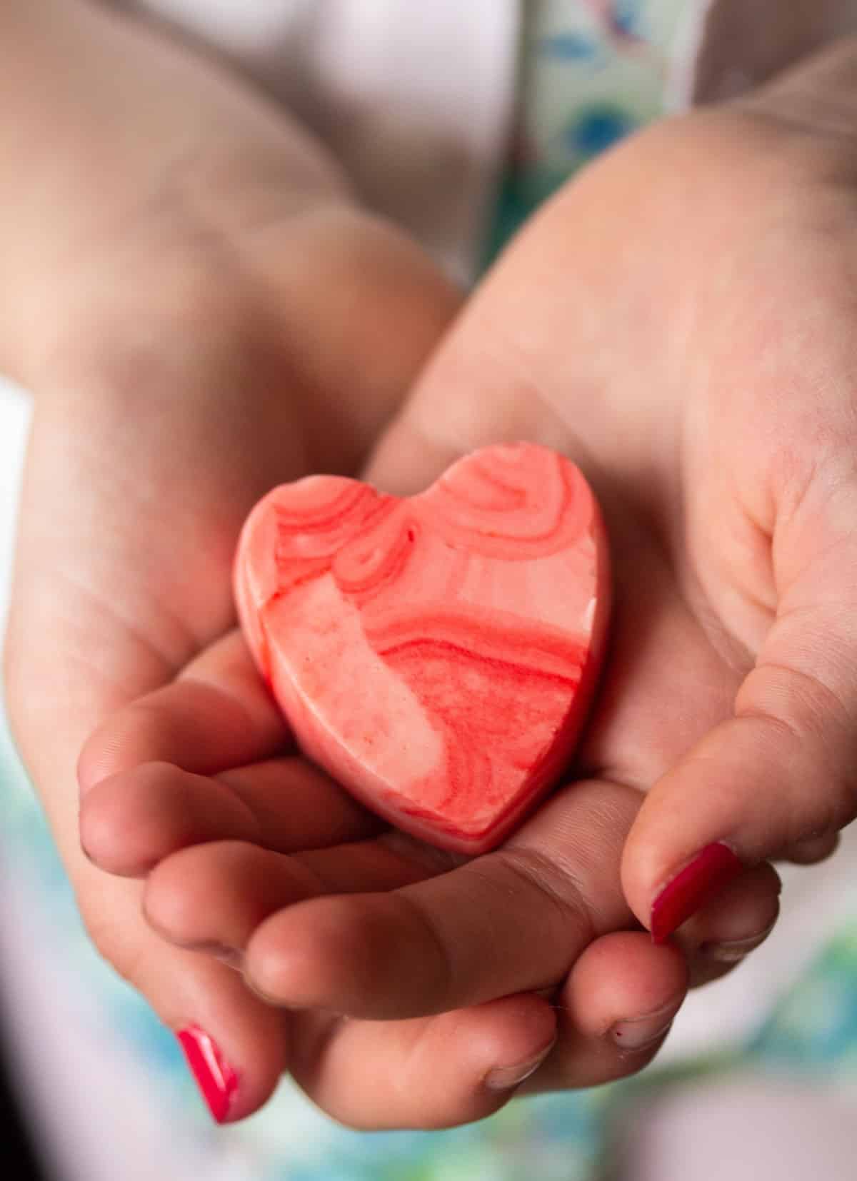girl's hands holding a heart-shaped piece of pink fudge.