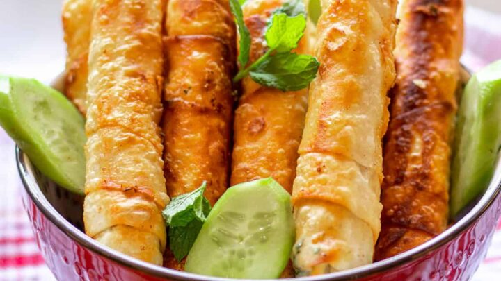 many long golden brown turkish cheese rolls in a red bowl.