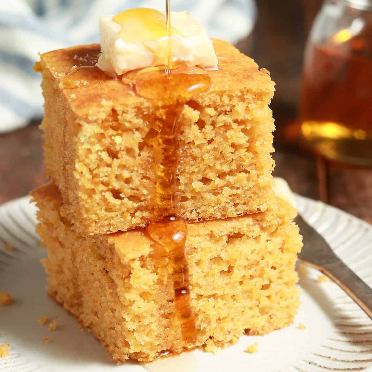 two stapled pieces of cornbread with butter on top, drizzled with honey.