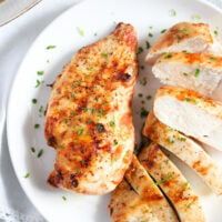 two pieces of air fryer chicken breast on a plate, one of them thickly sliced.