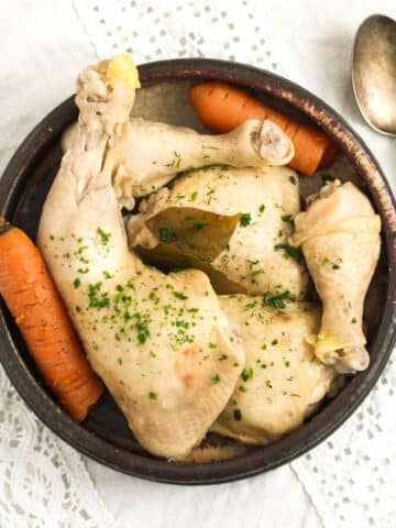 overhead view of boiled chicken legs and carrots in a bowl with a spoon beside it.