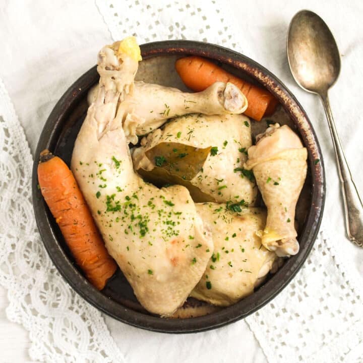 overhead view of boiled chicken legs and carrots in a bowl with a spoon beside it.