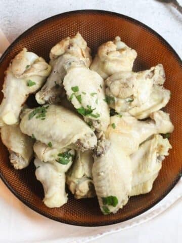 overhead view of a brown plate full of boiled chicken wings sprinkled with parsley.