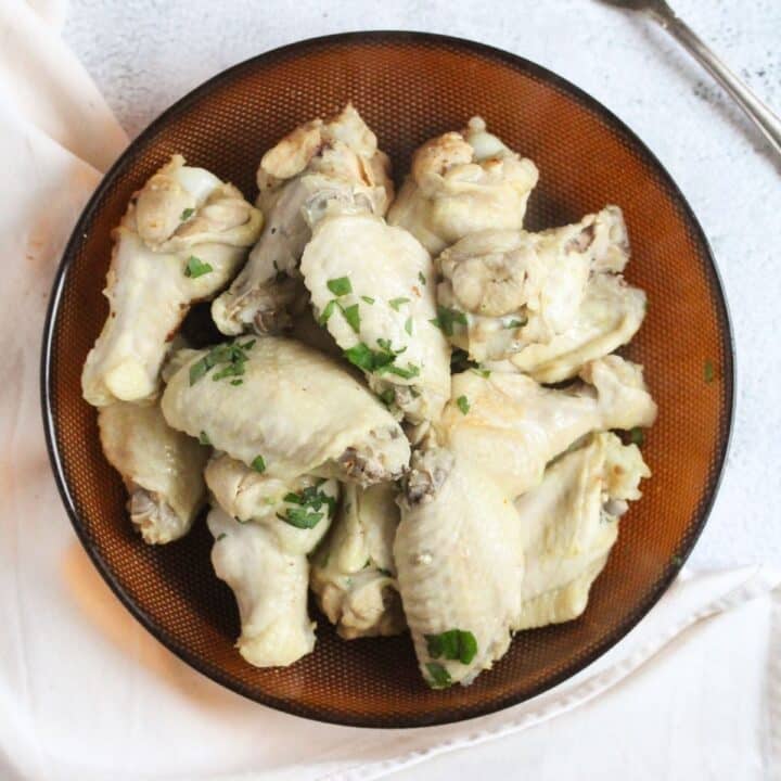 overhead view of a brown plate full of boiled chicken wings sprinkled with parsley.