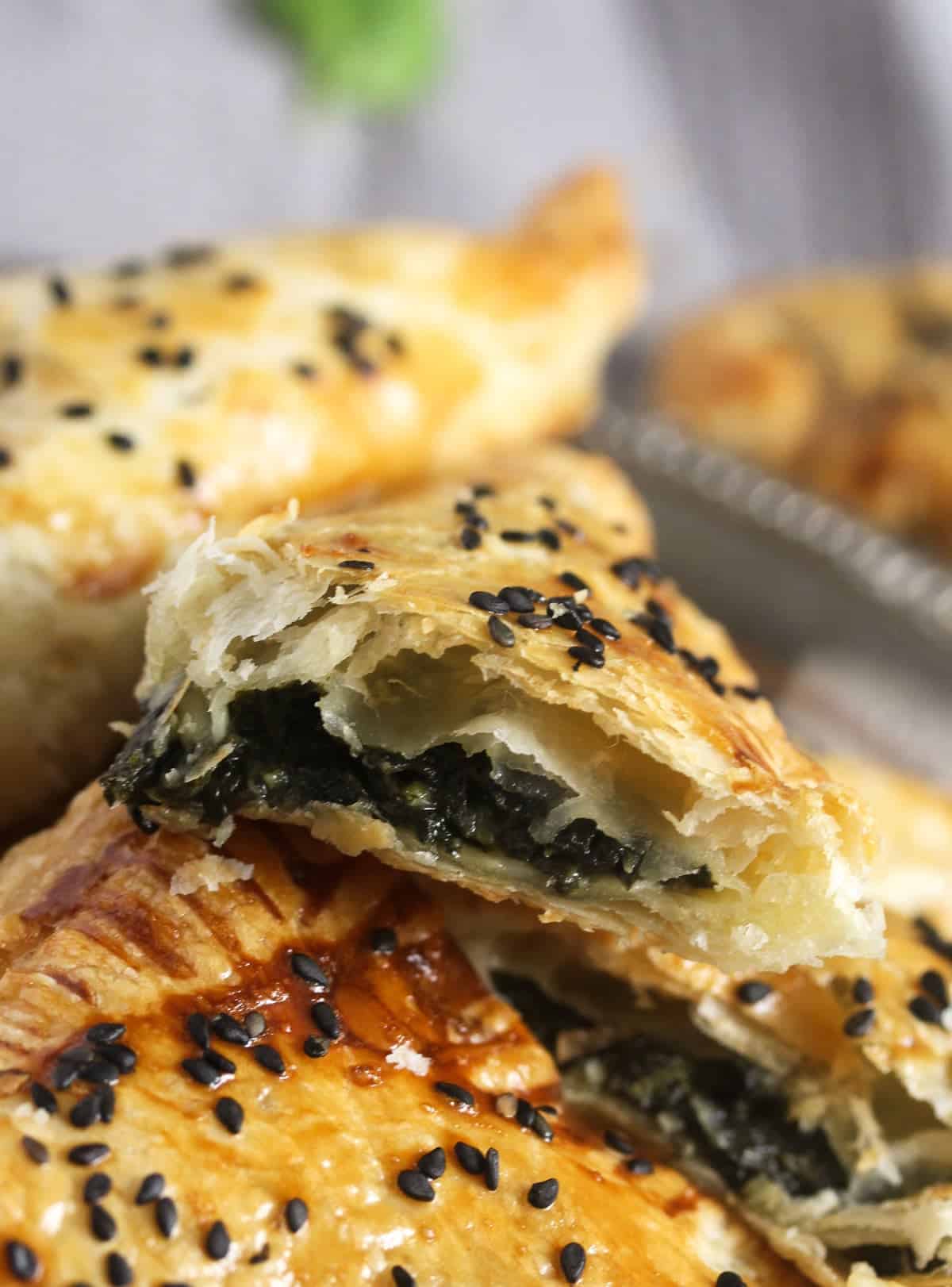a mini spanakopita triangle sprinkled with black sesame seeds showing the filling.