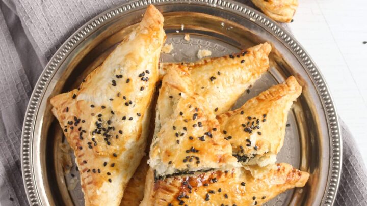 overhead view of several spinach feta spanakopita triangles on a silver plate.