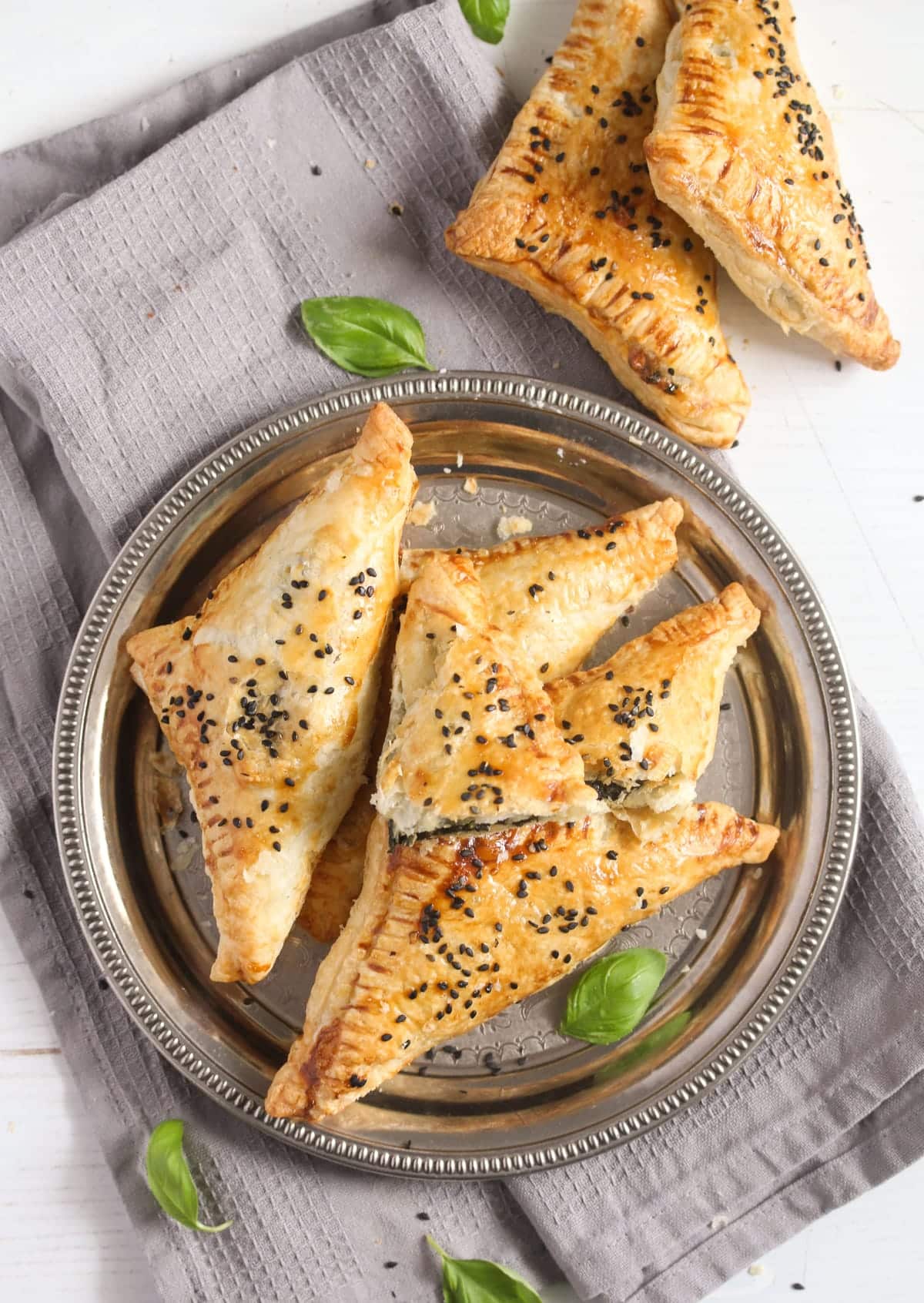 overhead view of several spinach feta spanakopita triangles on a silver plate.