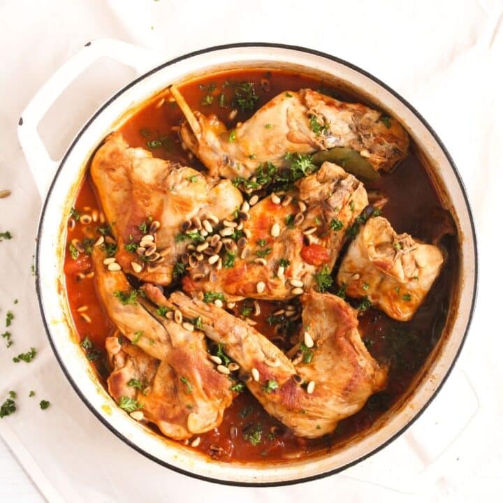 italian rabbit stew sprinkled with parsley in a white dutch oven.