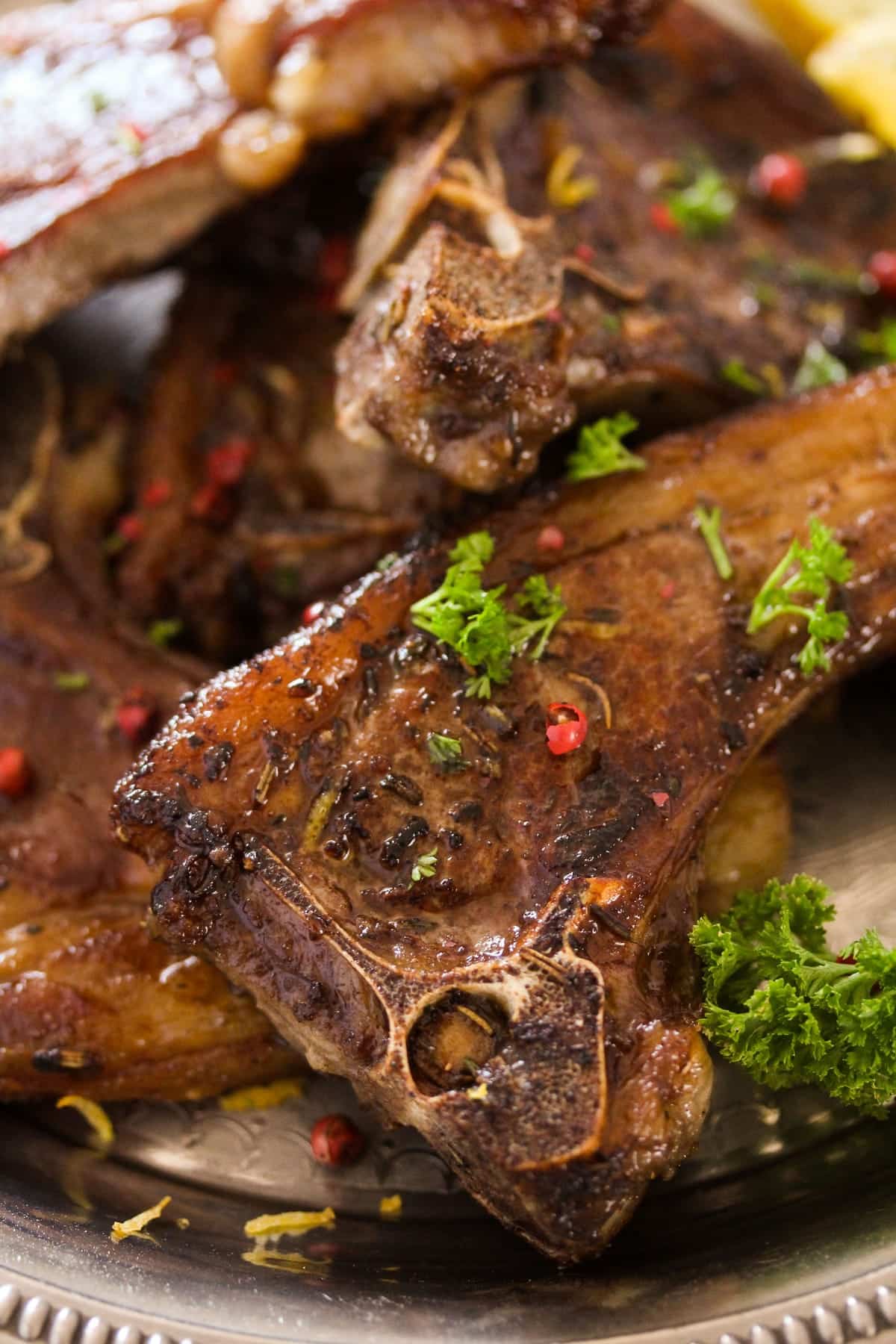 close up of lamb lollipops sprinkled with parsley and red peppercorns.