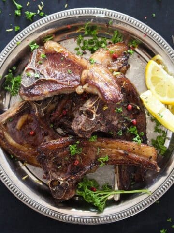 overhead view of a silver plate full of lamb lollipops and two lemon wedges.
