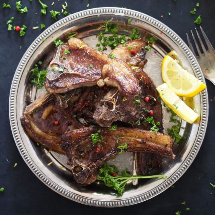 overhead view of a silver plate full of lamb lollipops and two lemon wedges.