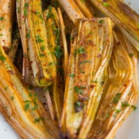 close up of golden roasted leeks sprinkled with parsley.
