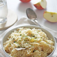 white bowl full of german sauerkraut with cut apple pieces and a spoon behind it.