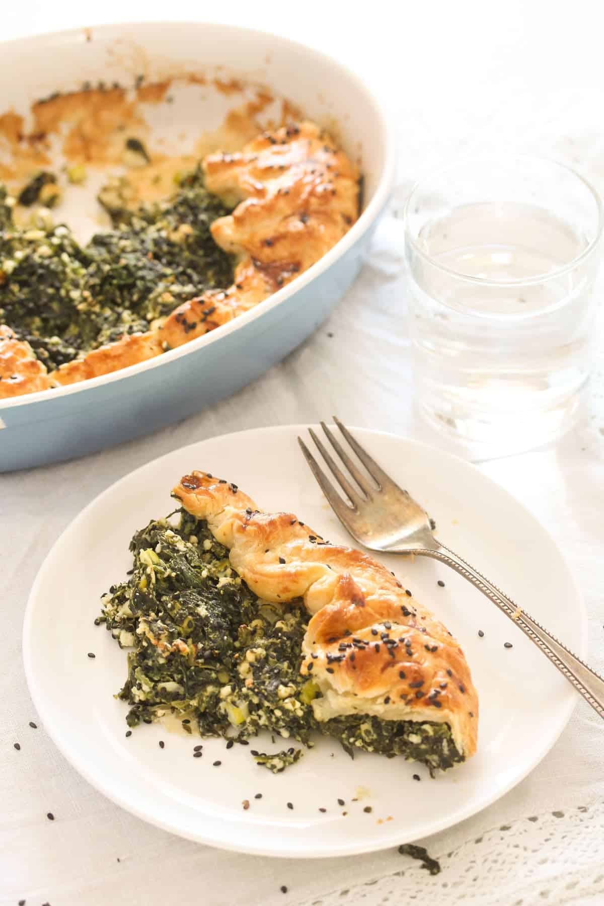 plate with a slice of spinach feta pie, the whole pie in a dish behind it.