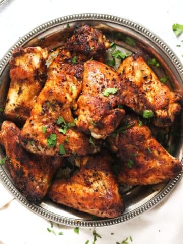 baked whole chicken wings on a silver plate sprinkled with parsley.