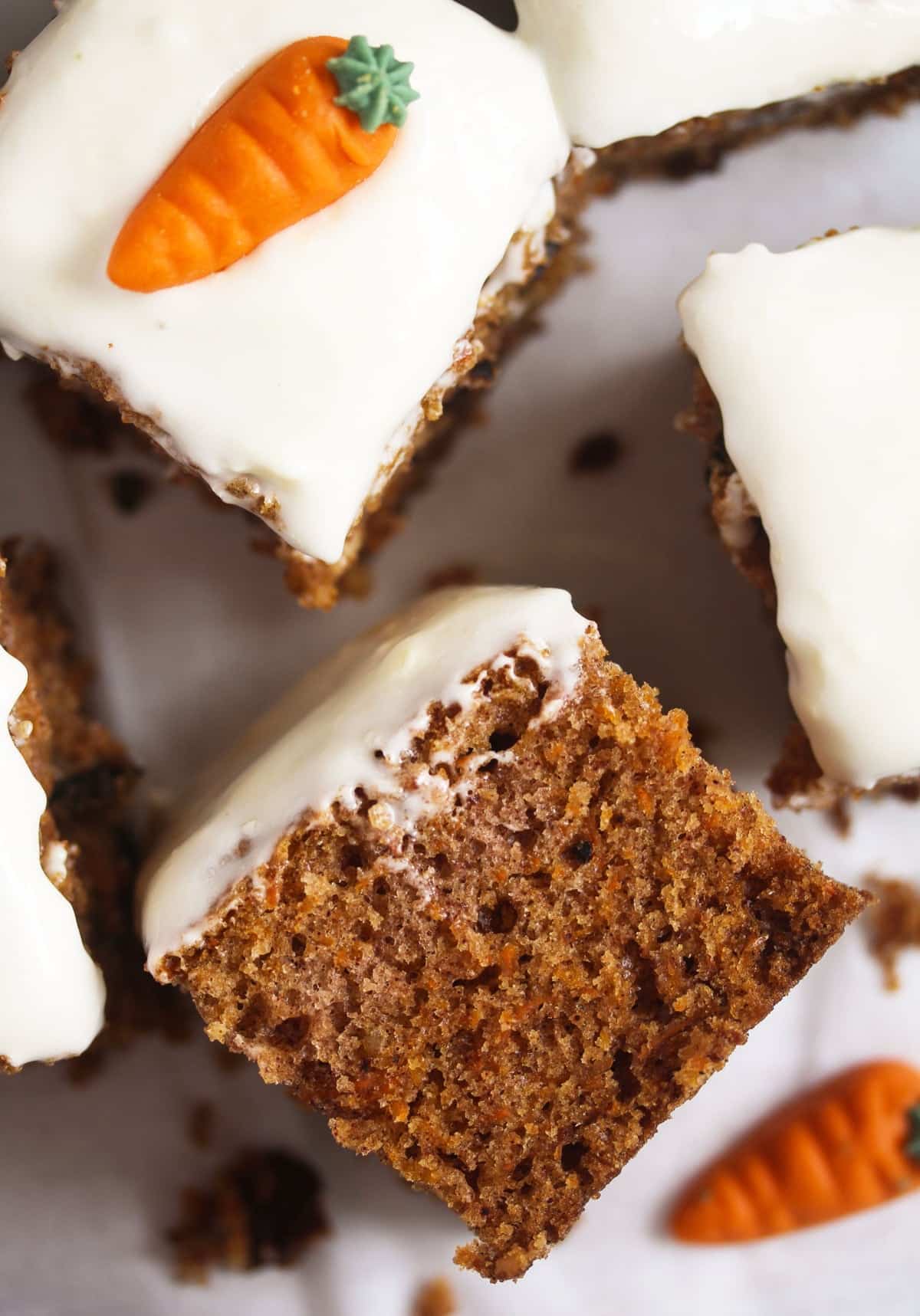close up of a square of carrot cake showing the moist crumb, another frosted piece beside it.