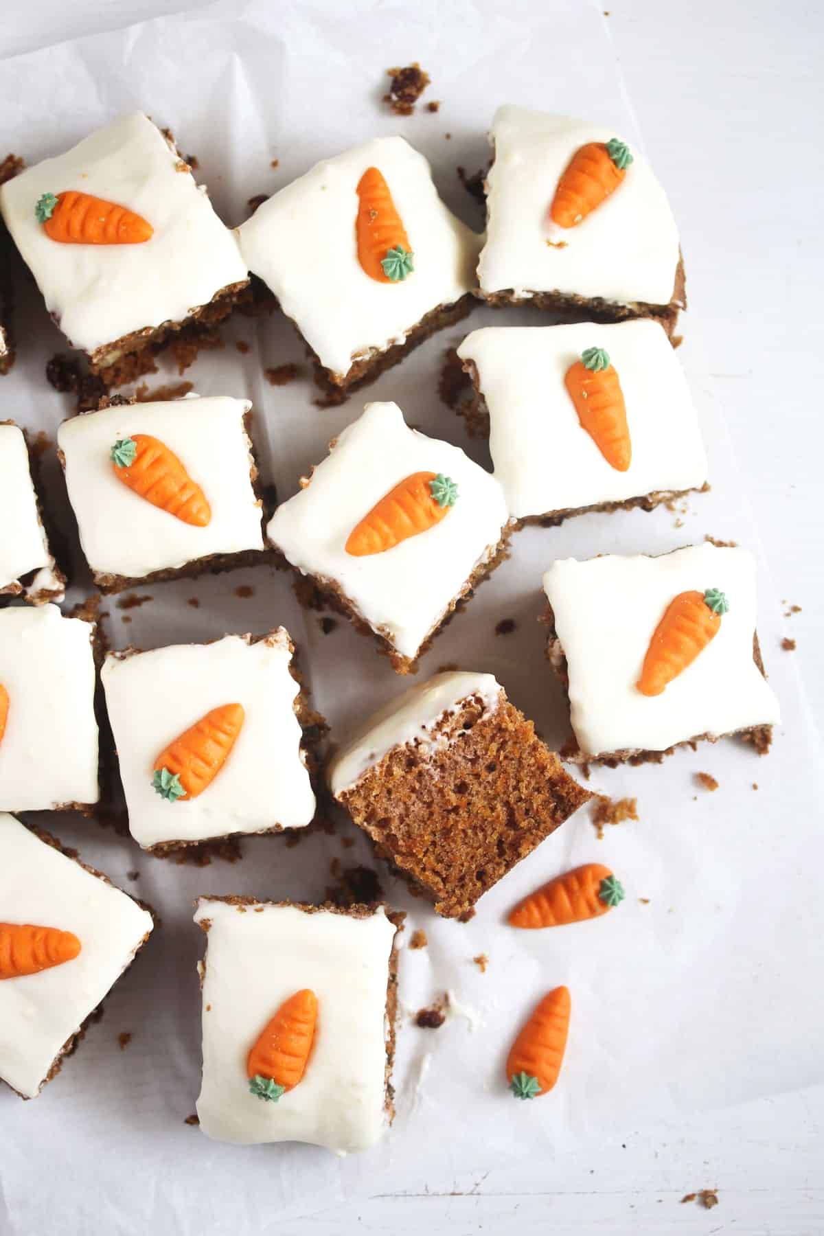 overhead view of many squares of carrot cake frosted and decorated with marzipan carrots.