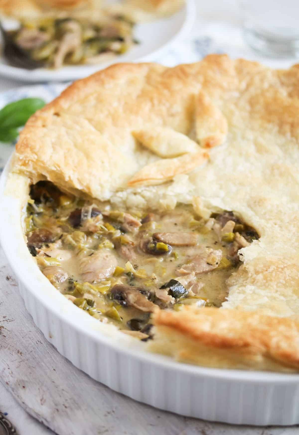 chicken pie with leeks and mushrooms in a ceramic dish with a piece of pastry missing on top.