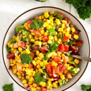 overhead view of a bowl with corn, tomatoes and herbs, half an avocado beside it.