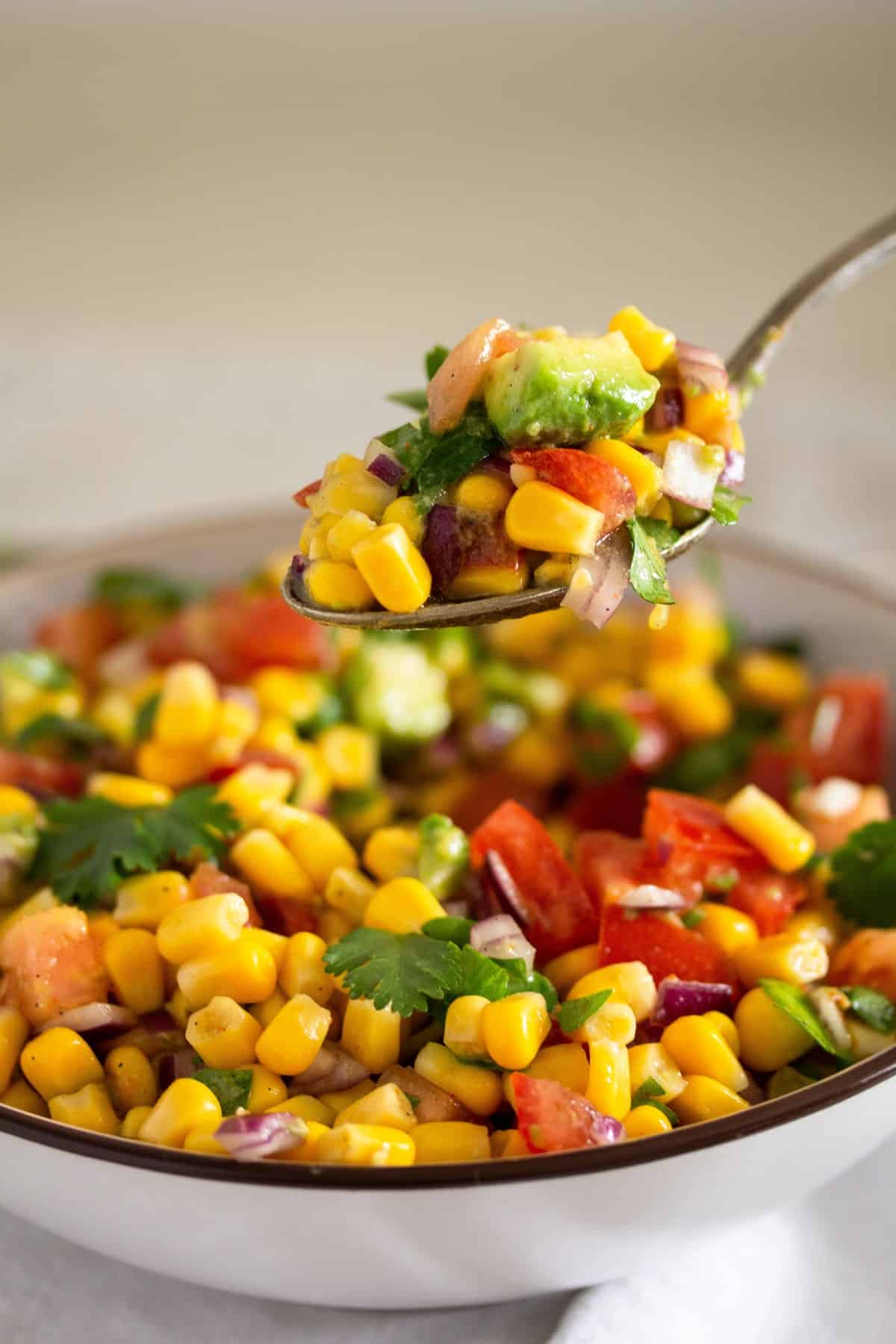 lifting corn salad with a spoon from a full bowl.