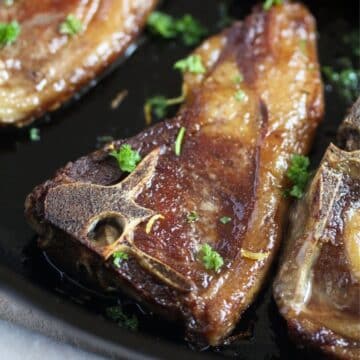 close up of cast-iron skillet fried lamb chops sprinkled with parsley.
