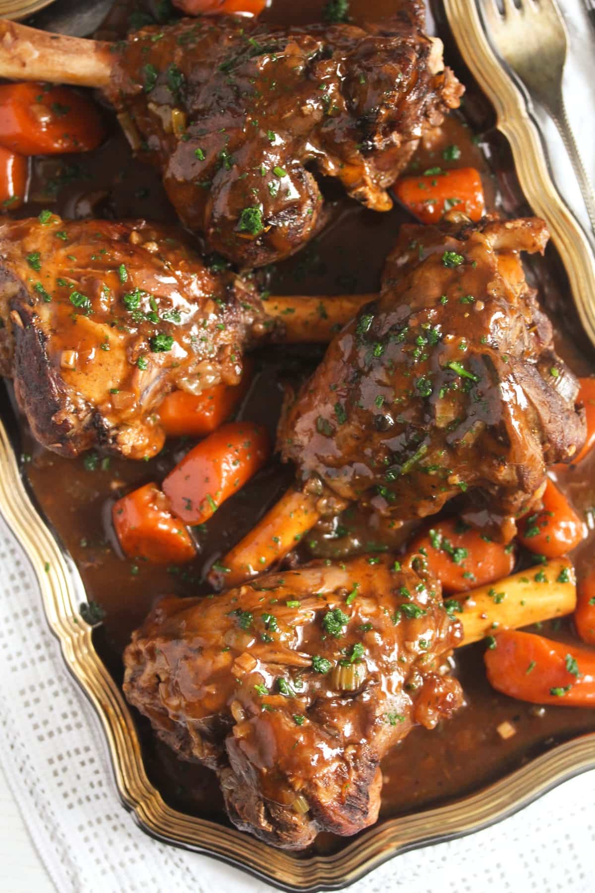 four shanks of lamb with carrots and gravy on a platter.