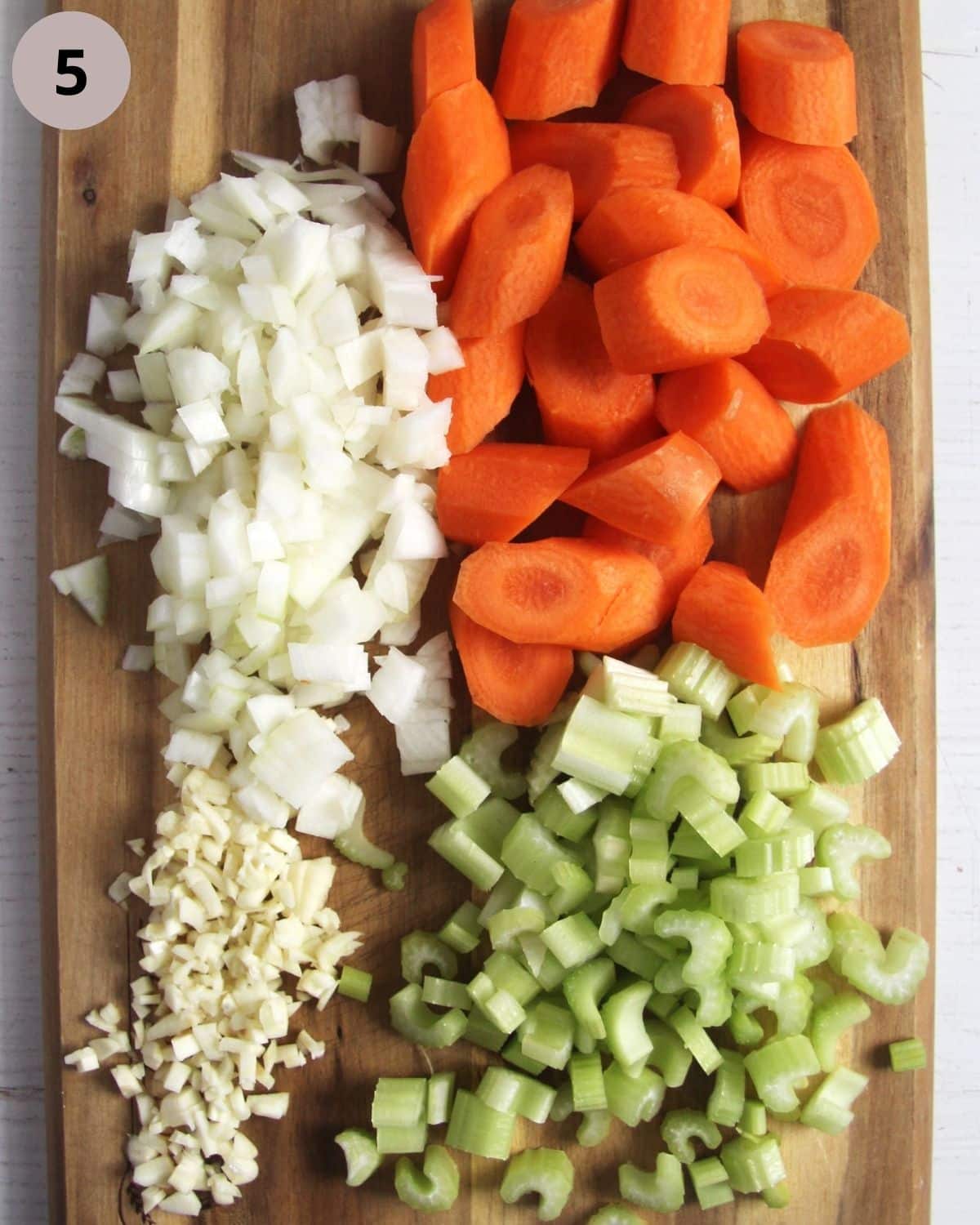 chopped carrots, onions, garlic and celery on a wooden board.
