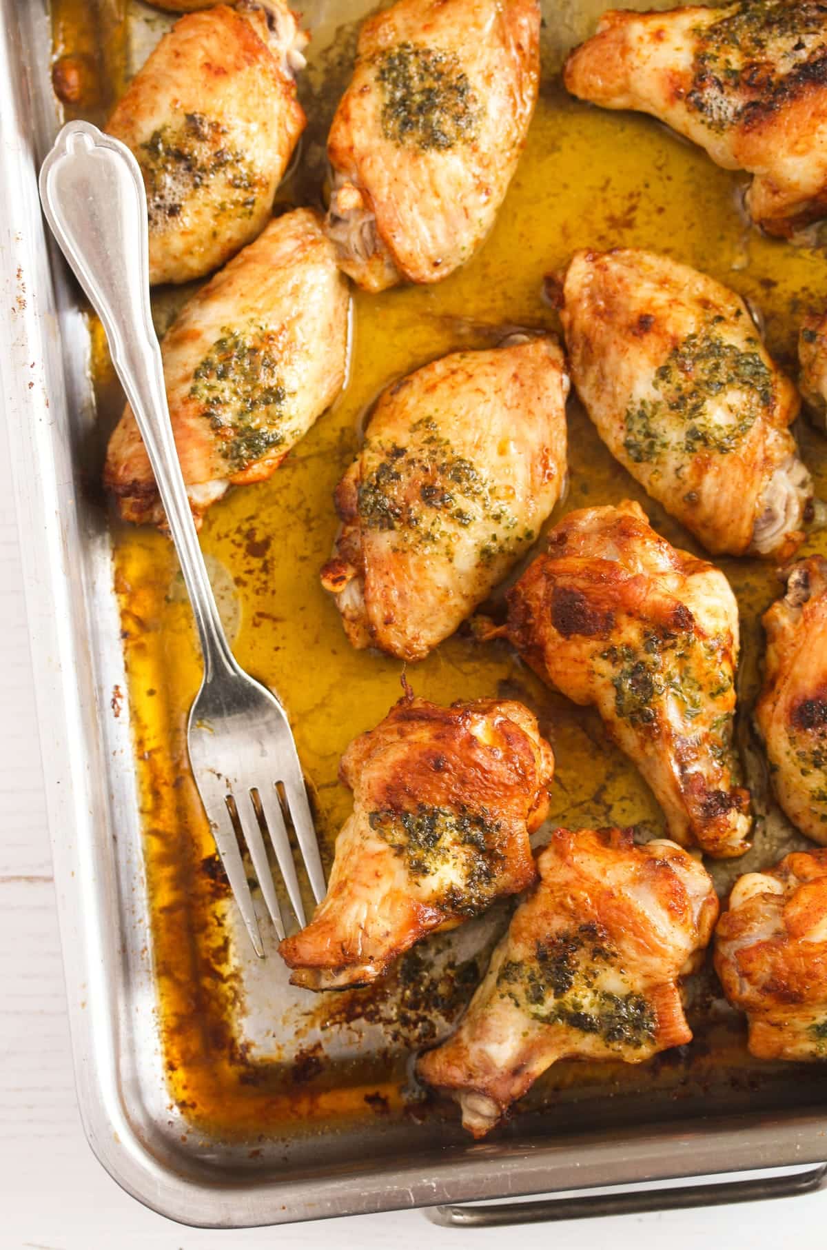 close image of a baking tin with juicy chicken wings and a fork.