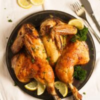 overhead image of a spatchcocked chicken on a plate with lemons around it.