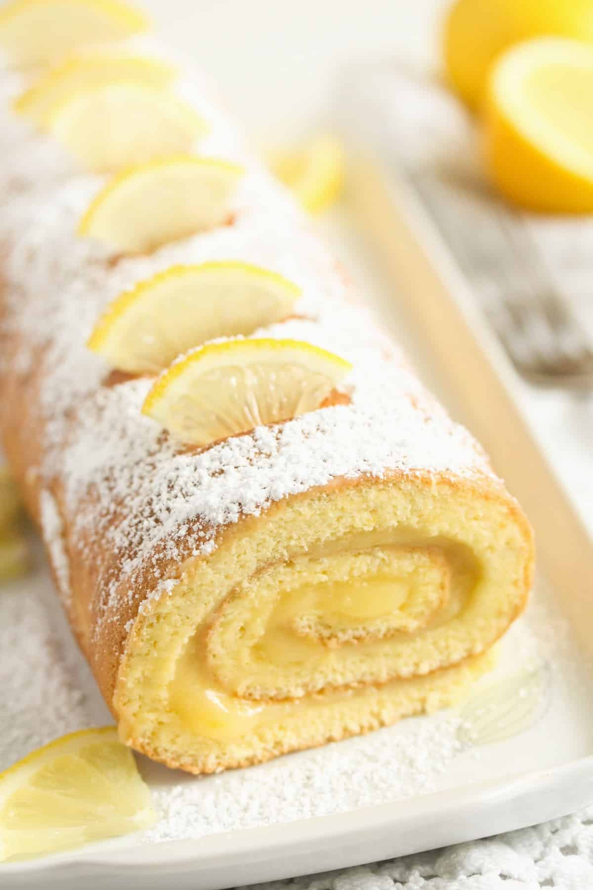 lemon cake roll sprinkled with icing sugar and topped with small lemon slices.
