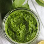 pesto in a jar, half a lemon and fresh lovage leaves on the table.