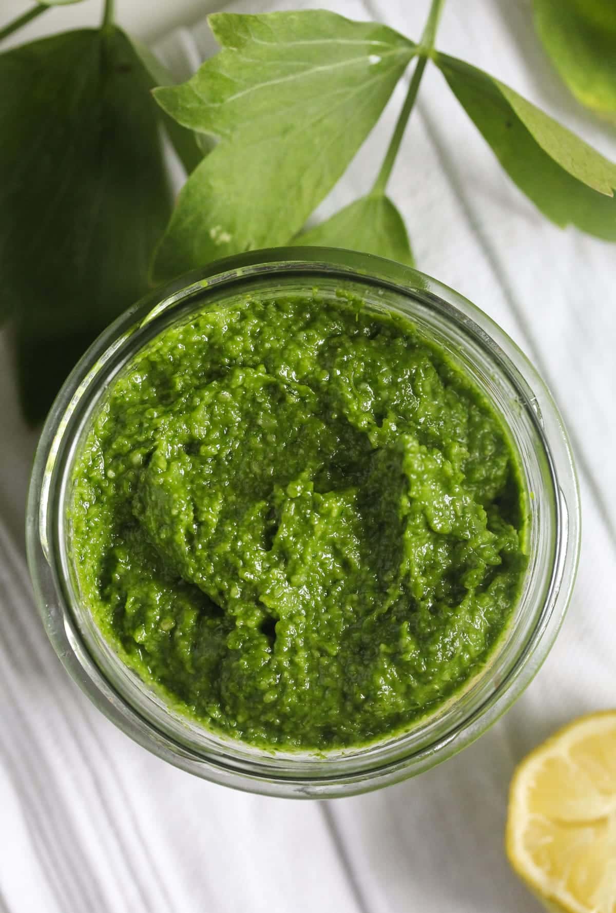 pesto in a jar, half a lemon and fresh lovage leaves on the table.