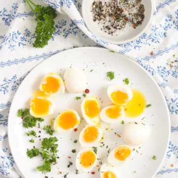 bright yellow halved eggs from the quail on a white plate with a bowl of seasoning.