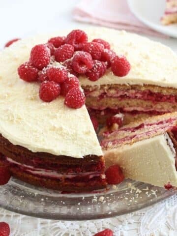 raspberry and white chocolate cake decorated with fresh berries on a platter.