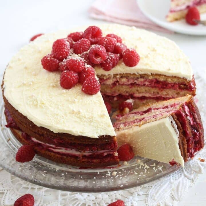 raspberry and white chocolate cake decorated with fresh berries on a platter.
