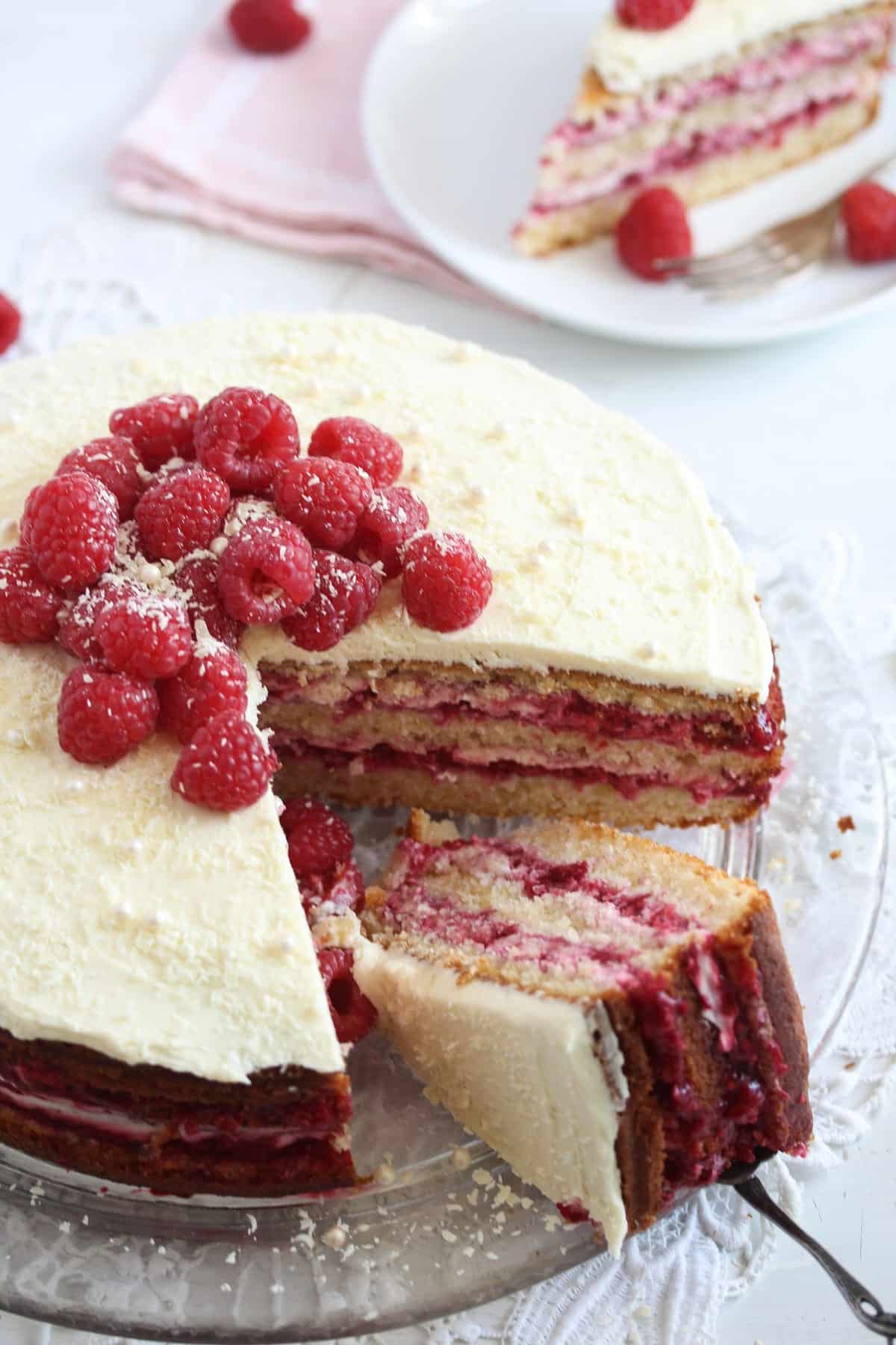 long image of sliced cake with raspberry filling and berries on top.