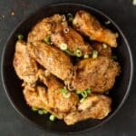 salt and pepper chicken wings in a black bowl on a black board.