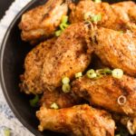 close up of a plate with many crispy salt and pepper chicken wings sprinkled with green onions.