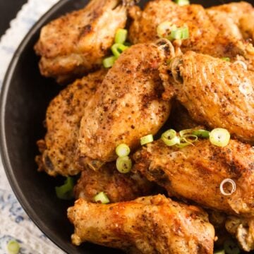 close up of a plate with many crispy salt and pepper chicken wings sprinkled with green onions.