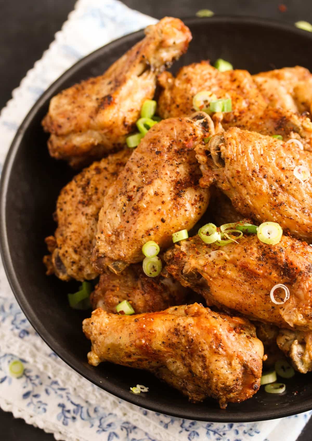 close up of a plate with many crispy salt and pepper chicken wings sprinkled with green onions.