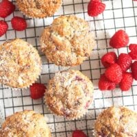 many muffins with white chocolate and fresh raspberries on a rack.