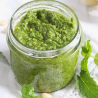 jar of basil mint pesto with pine nuts and mint leaves around it.