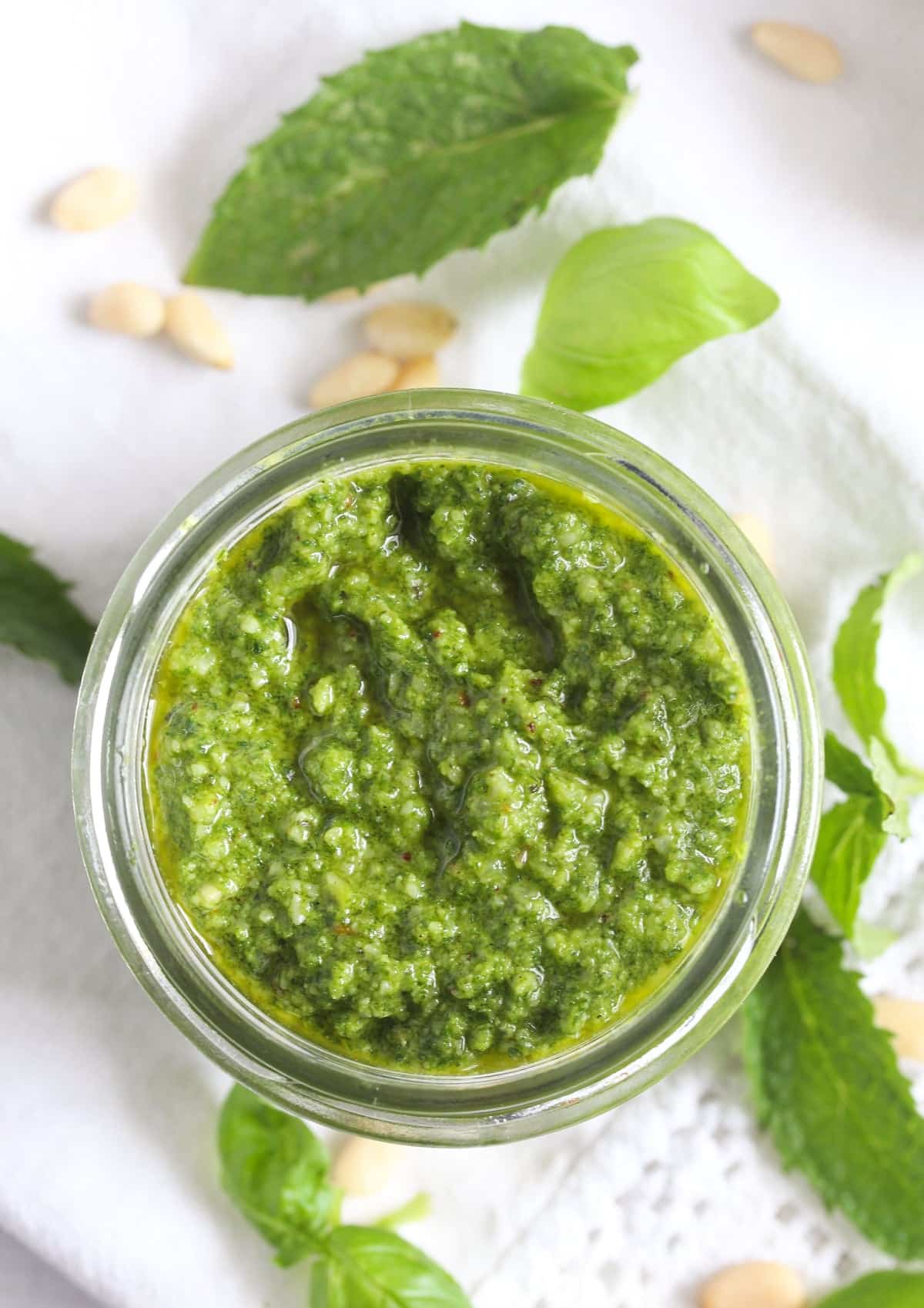overhead view of pesto in a jar, mint and basil leaves aroud it.