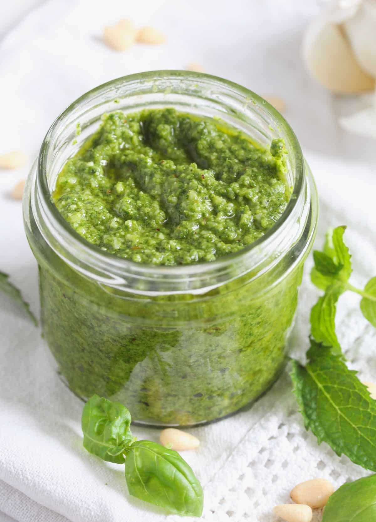 jar of basil mint pesto with pine nuts and mint leaves around it.